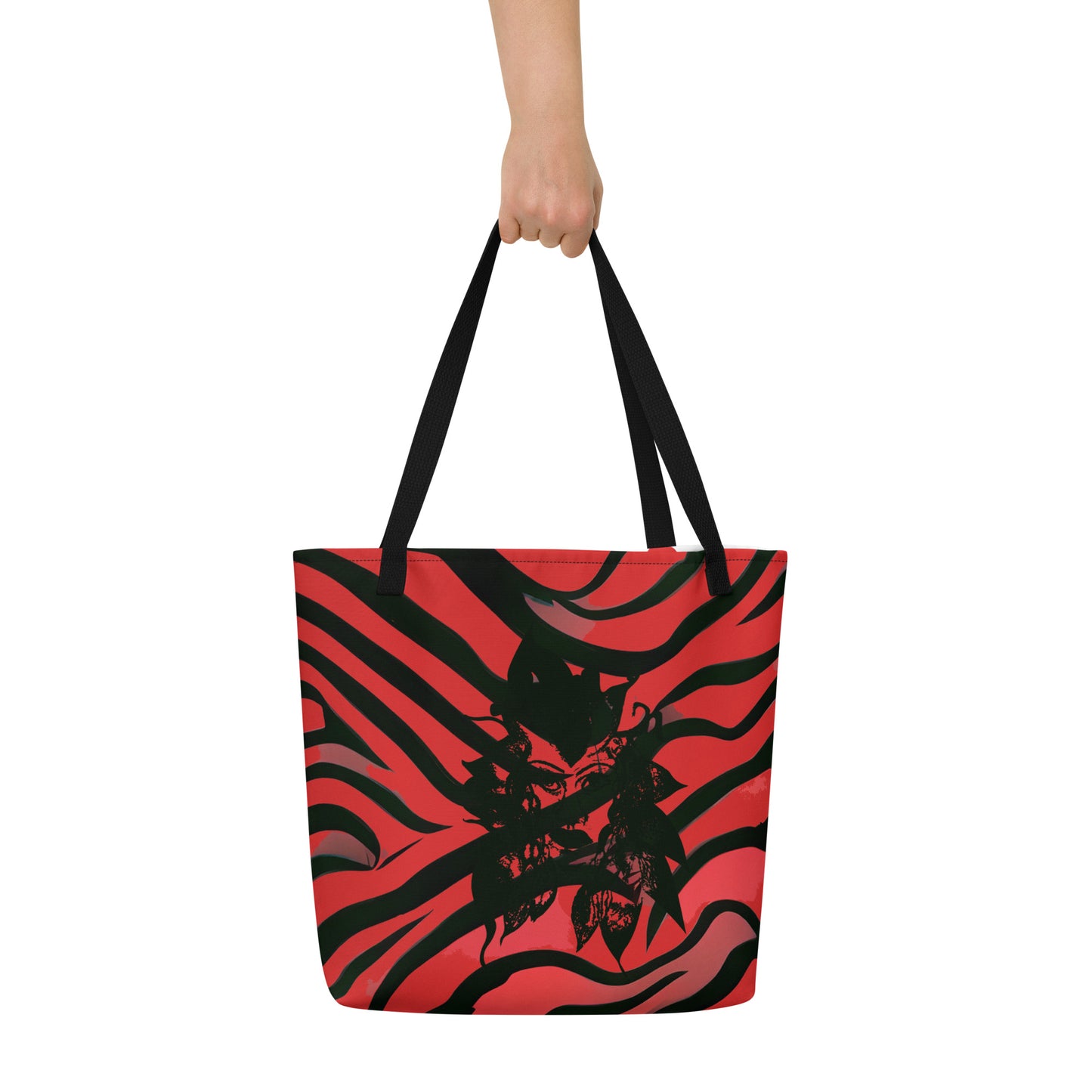 The hand holding a large red and black tote bag from Kloe Store featuring a bold artistic face design and abstract swirling patterns, with black straps, perfect for trendy and functional everyday use, detail view.