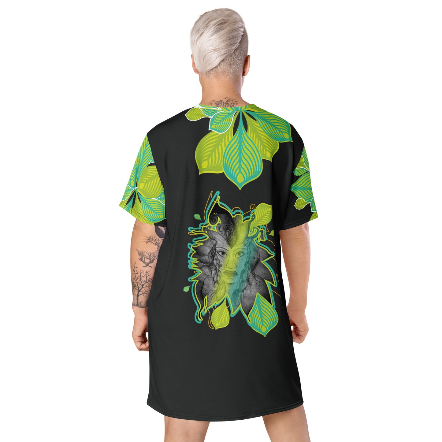 Back view of an all-over print K.L.O.E. t-shirt dress featuring vibrant green and yellow leaf patterns framing a detailed black and gray hand-drawn face design, celebrating individuality, modern bohemian style, and self-expression, worn by a model.