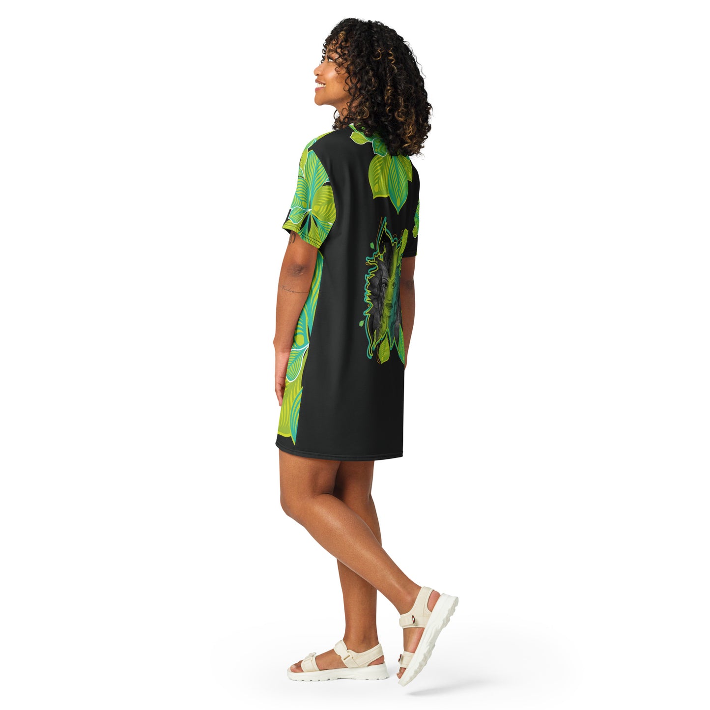 Back view of an all-over print K.L.O.E. t-shirt dress featuring vibrant green and yellow leaf patterns framing a detailed black and gray hand-drawn face design, celebrating individuality, modern bohemian style, and self-expression, worn by a model.