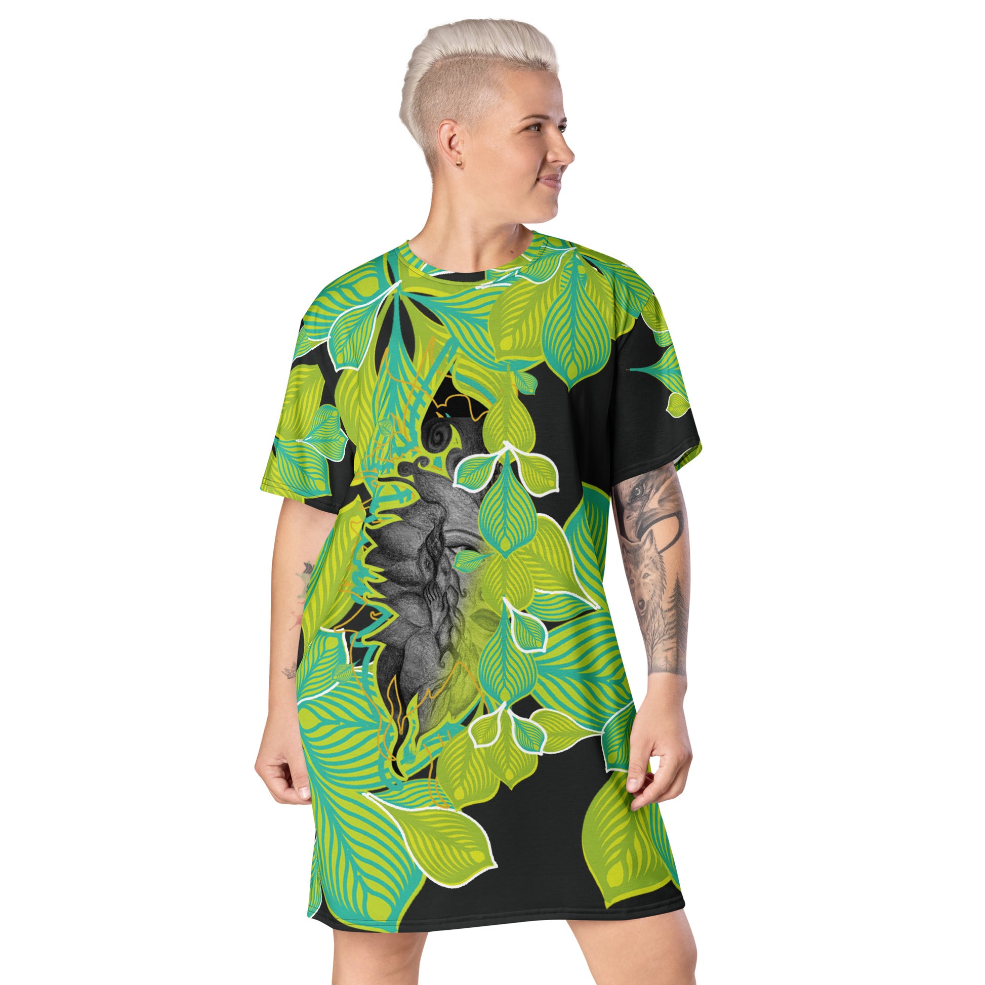 A model wearing all-over print K.L.O.E. t-shirt dress featuring vibrant green and yellow leaf patterns framing a detailed black and gray hand-drawn face design, highlighting individuality, self-expression, and modern bohemian style.