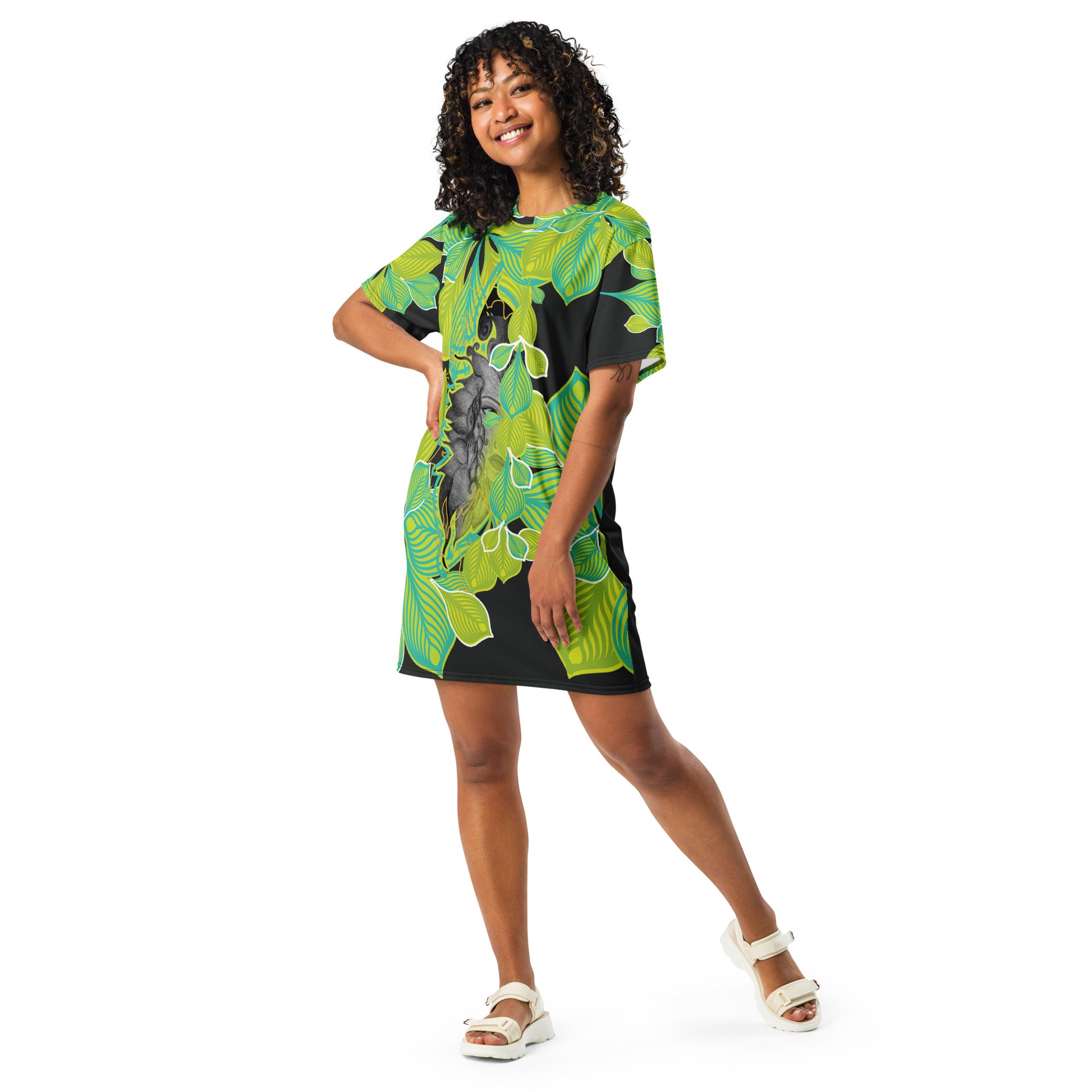 A model wearing all-over print K.L.O.E. t-shirt dress featuring vibrant green and yellow leaf patterns framing a detailed black and gray hand-drawn face design, highlighting individuality, self-expression, and modern bohemian style.