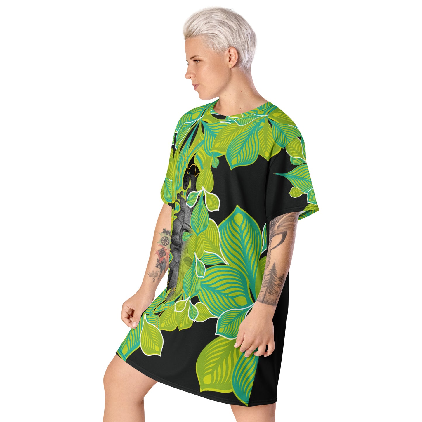 A model wearing all-over print K.L.O.E. t-shirt dress featuring vibrant green and yellow leaf patterns framing a detailed black and gray hand-drawn face design, highlighting individuality, self-expression, and modern bohemian style.