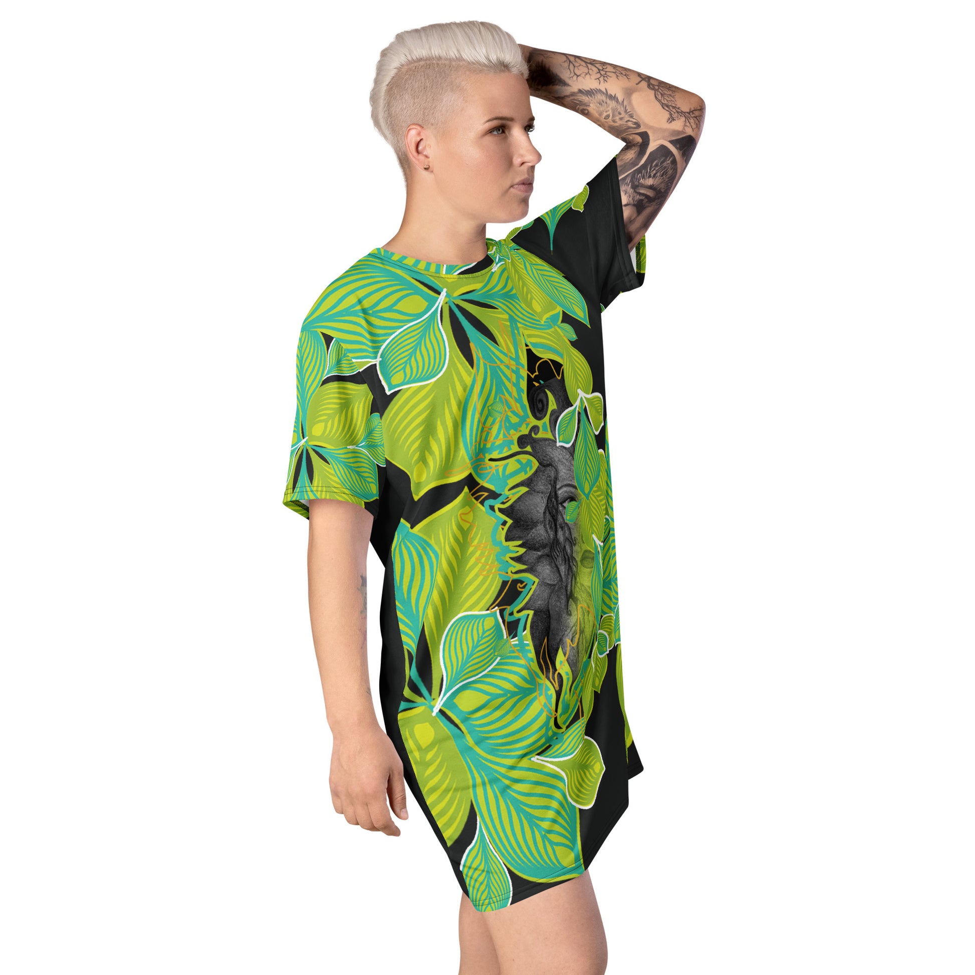 A model wearing all-over print K.L.O.E. t-shirt dress featuring vibrant green and yellow leaf patterns framing a detailed black and gray hand-drawn face design, highlighting individuality, self-expression, and modern bohemian style.