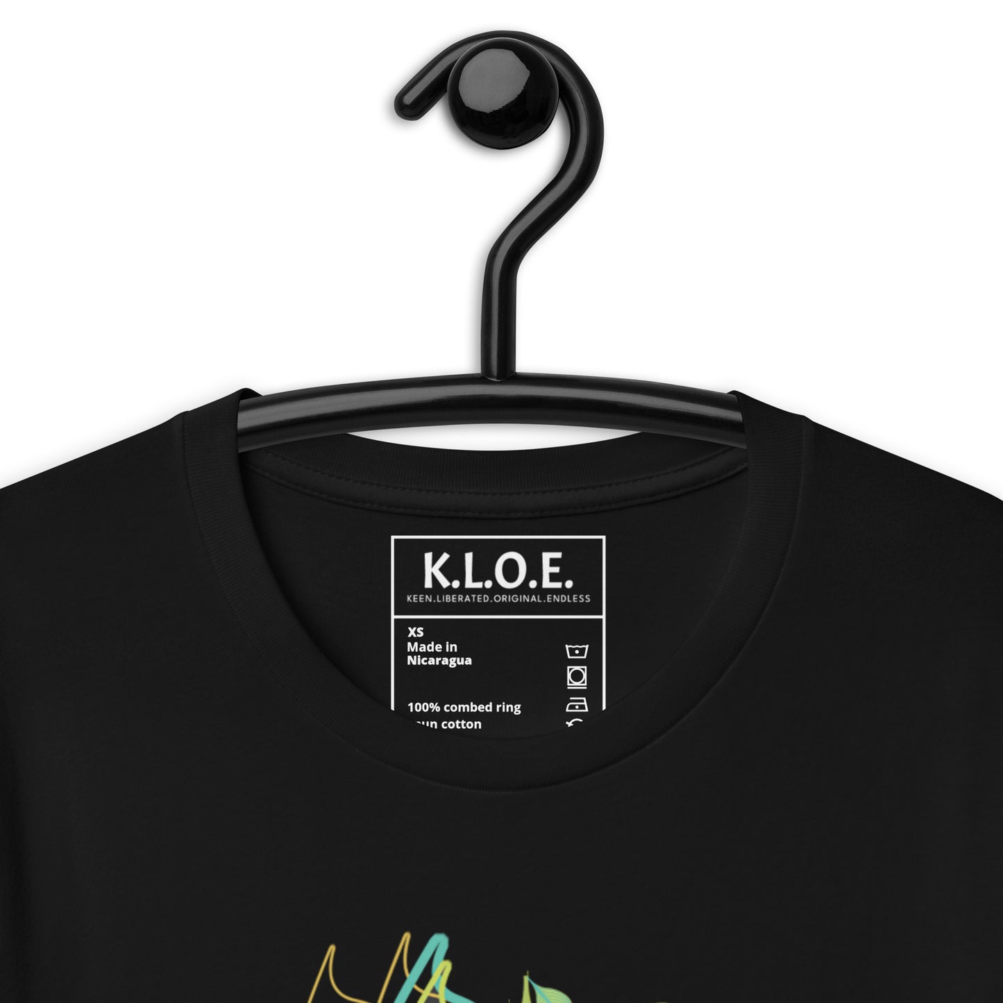 Detail view of the front side of black K.L.O.E. t-shirt with vibrant green and yellow leaf patterns framing a detailed hand-drawn face design. A modern bohemian style statement that celebrates individuality, artistic expression, and culturally inspired fashion, on a model.