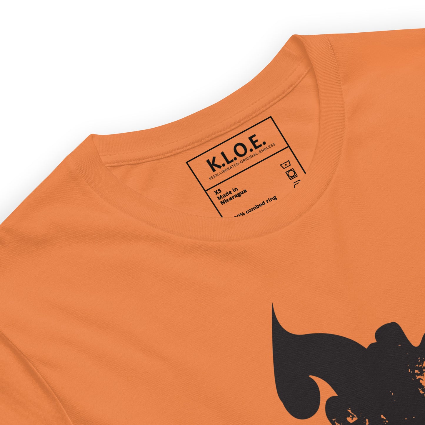 Detail view of orange K.L.O.E. T-shirt featuring a culturally inspired, hand-drawn black graphic of a bold, expressive face surrounded by intricate details, celebrating individuality and artistic self-expression in modern bohemian style fashion, the inside label view.