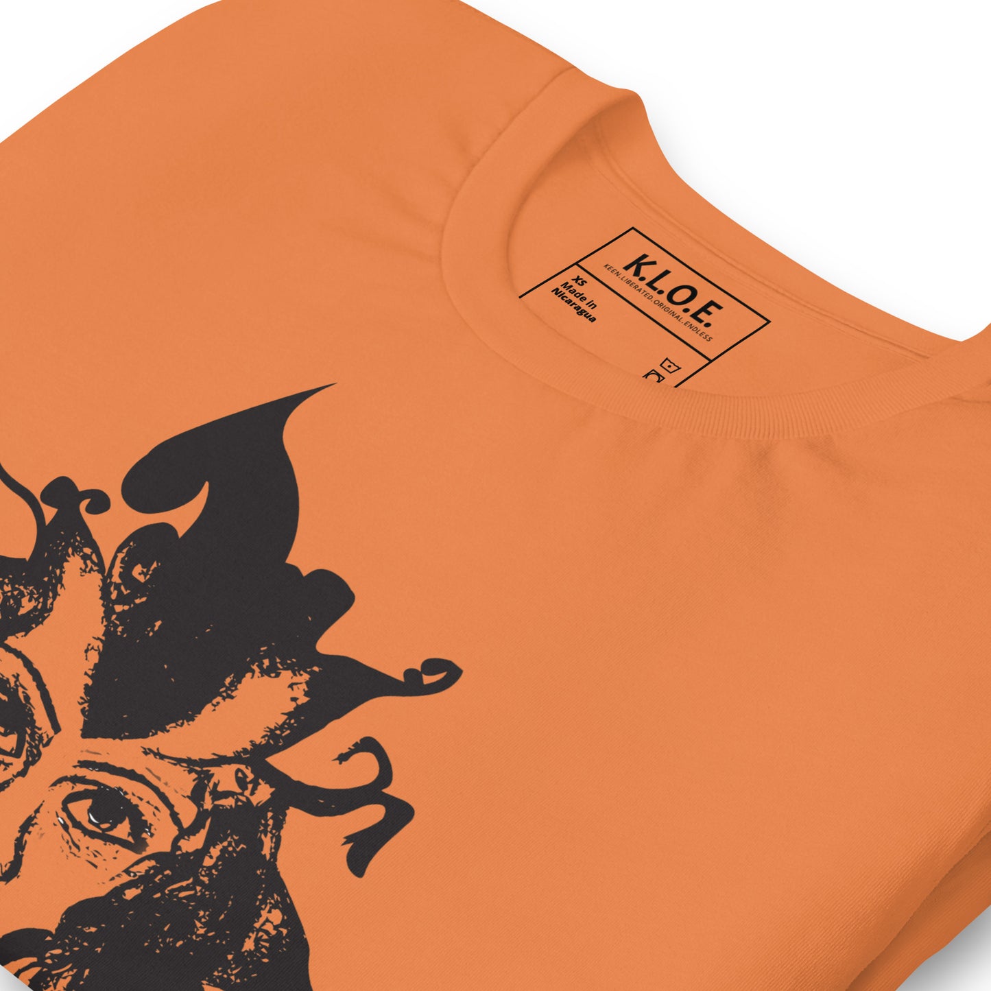 Detail view of orange K.L.O.E. T-shirt featuring a culturally inspired, hand-drawn black graphic of a bold, expressive face surrounded by intricate details, celebrating individuality and artistic self-expression in modern bohemian style fashion, the inside label view.