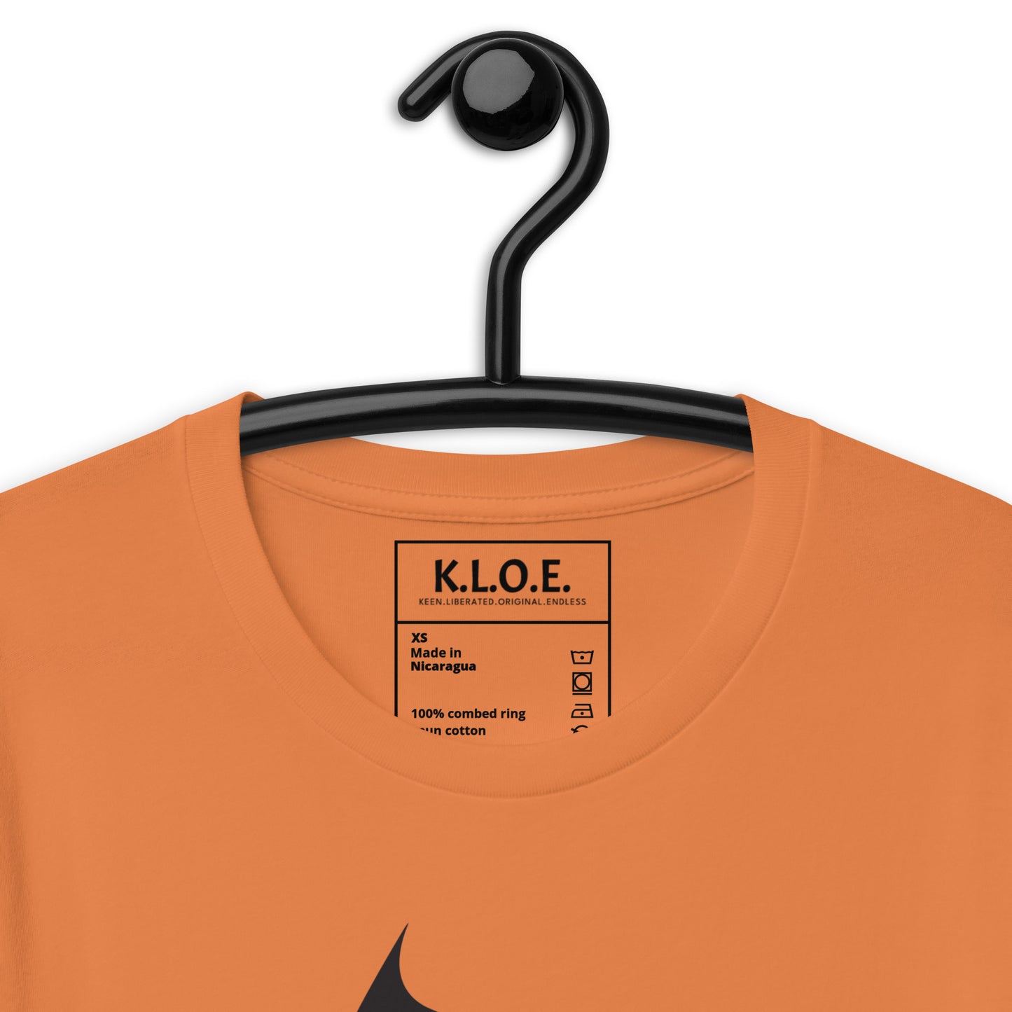 Detail view of orange K.L.O.E. T-shirt featuring a culturally inspired, hand-drawn black graphic of a bold, expressive face surrounded by intricate details, celebrating individuality and artistic self-expression in modern bohemian style fashion, the inside label view.