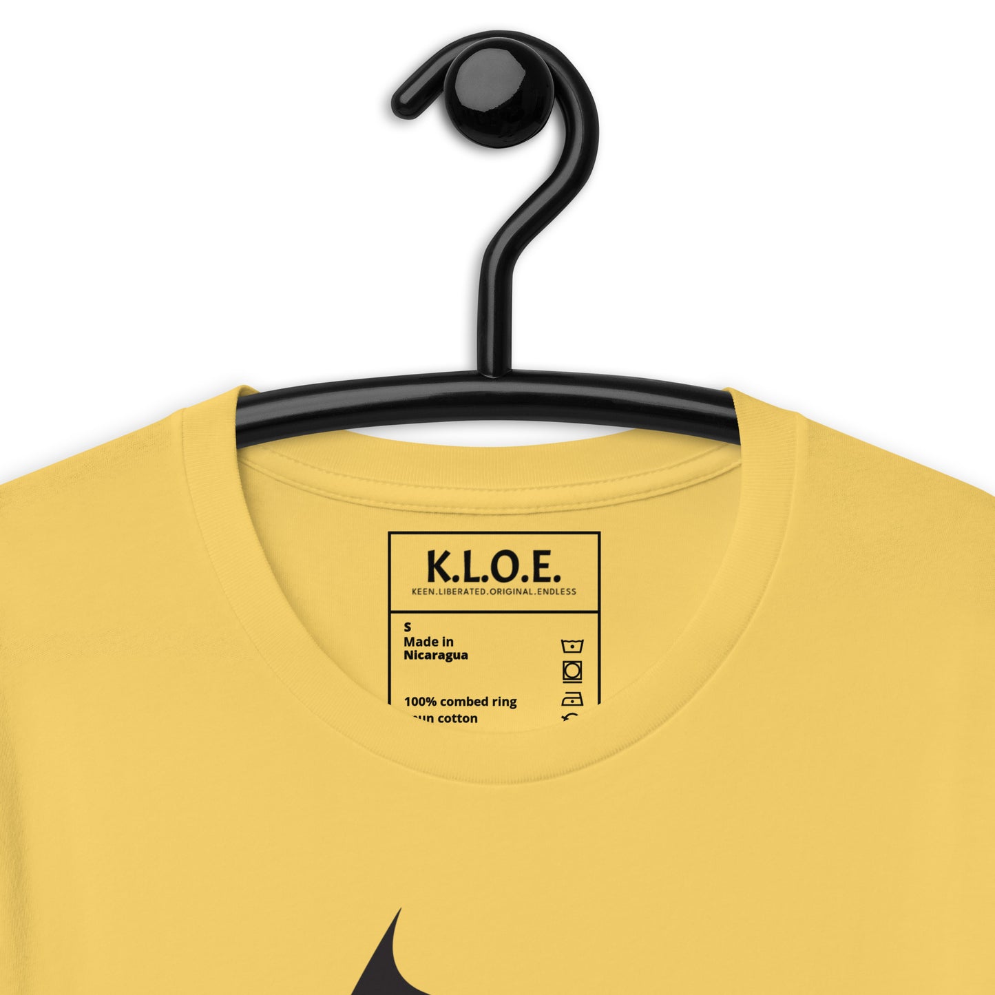 The view of the inside label of the yellow K.L.O.E. T-shirt featuring a culturally inspired, hand-drawn black graphic of a bold, expressive face surrounded by intricate details, celebrating individuality and artistic self-expression in modern bohemian style fashion.